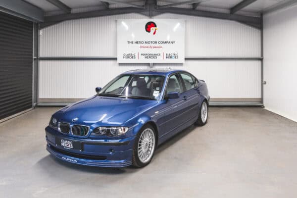 Front quarter view of a BMW E46 Alpina in metallic blue with decal stripes and 19