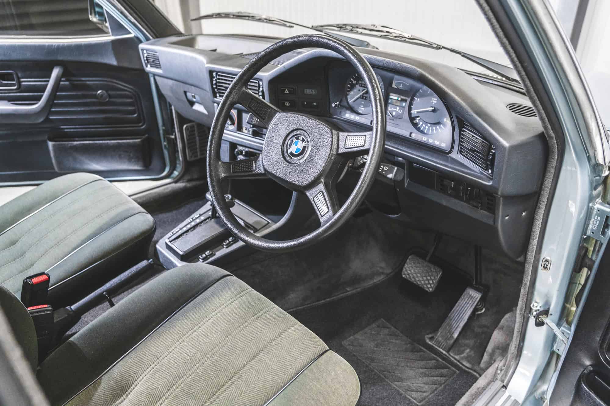 Drivers view of a four spoke steering wheel and dashboard of a BMW E28 525 Eta.