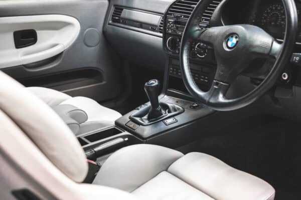 Driver side interior view of a BMW E36 M3 Coupe with Hell Grey Leather Vader seats and Black sports steering wheel.