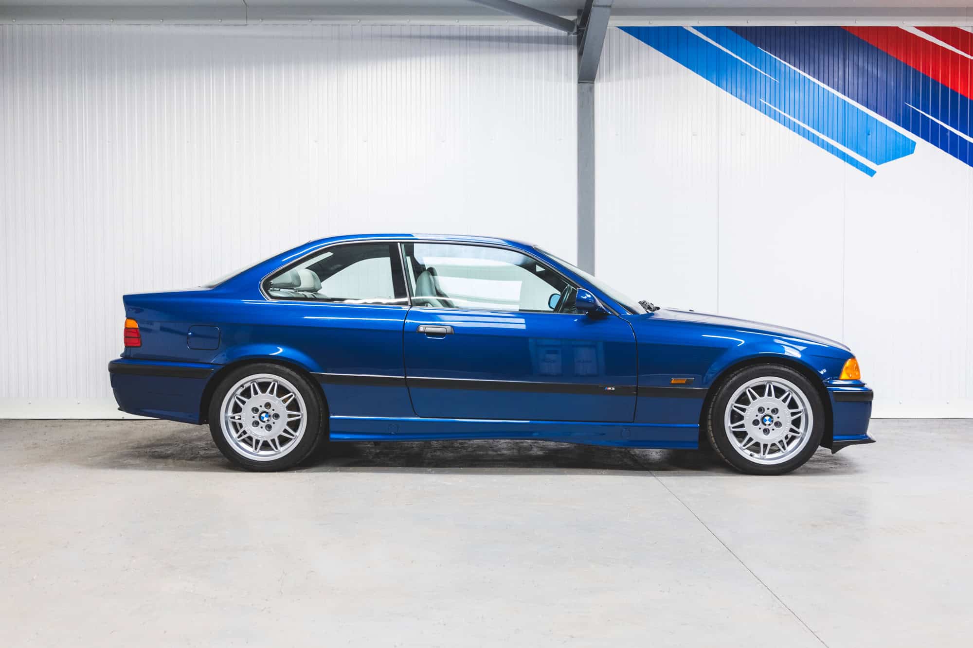 BMW E36 M3 offside exterior in Avus Blue with M Motorsport alloy wheels and green tinted windows.