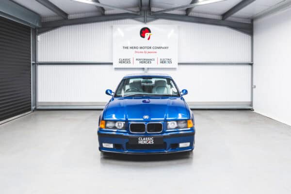 Front view of a BMW E36 M3 in Avus Blue under a Hero Motor Company sign.