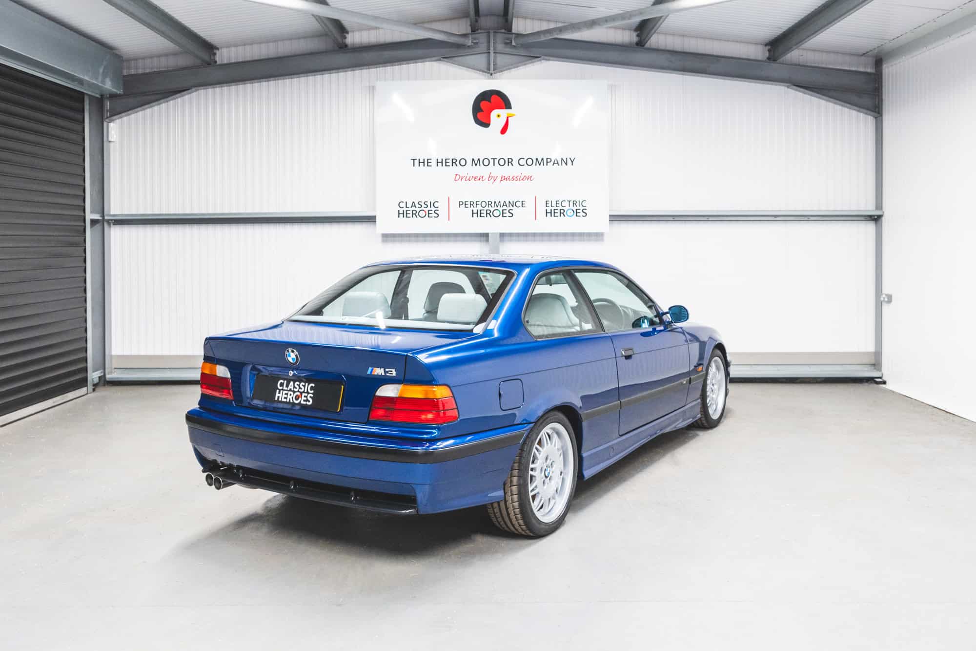 Rear quarter view of show winning BMW E36 M3 Coupe in Avis Blue with M3 body kit under a Hero Motor Company.