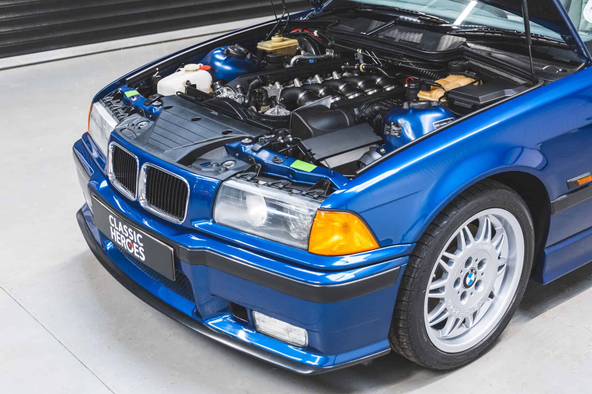 BMW E36 M3 in Avis Blue with bonnet up showing immaculate engine bay and headlights.