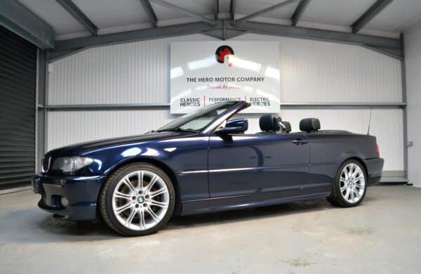 Nearside exterior roof down on Orient Blue Metallic 330ci alloy wheels and black leather headrests.