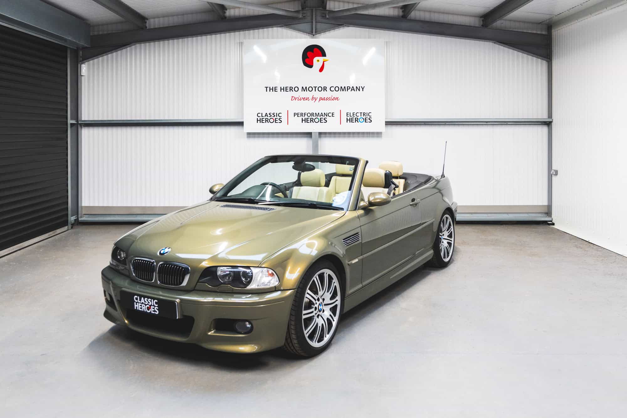 Front quarter view of a BMW E46 M3 Convertible with the roof down in Messing Metallic paint with under a Hero Motor Company sign.