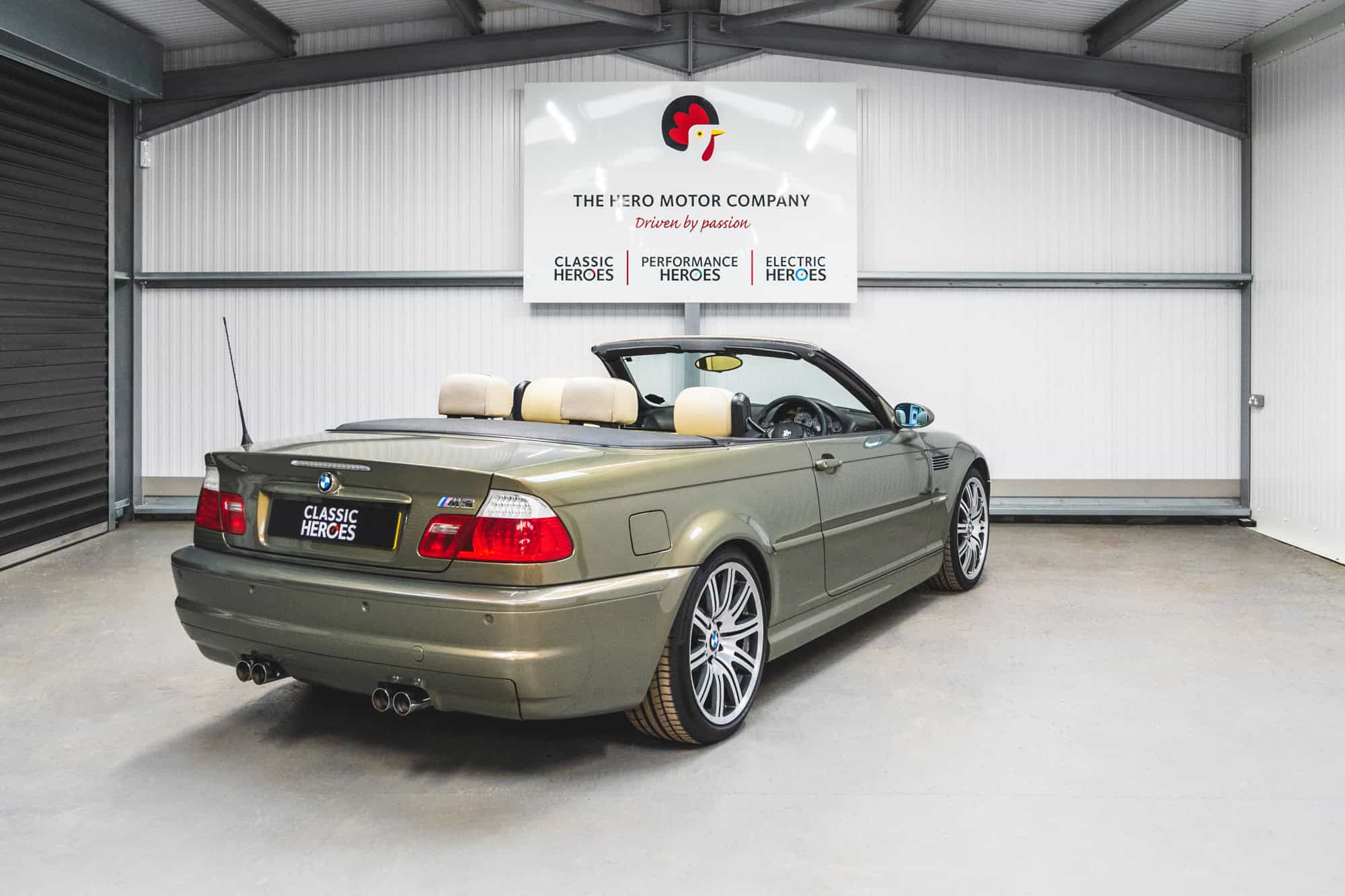 BMW E46 M3 Convertible in Messing Metallic green with cream leather interior and 19 inch wheels under a Hero Motor Company sign.