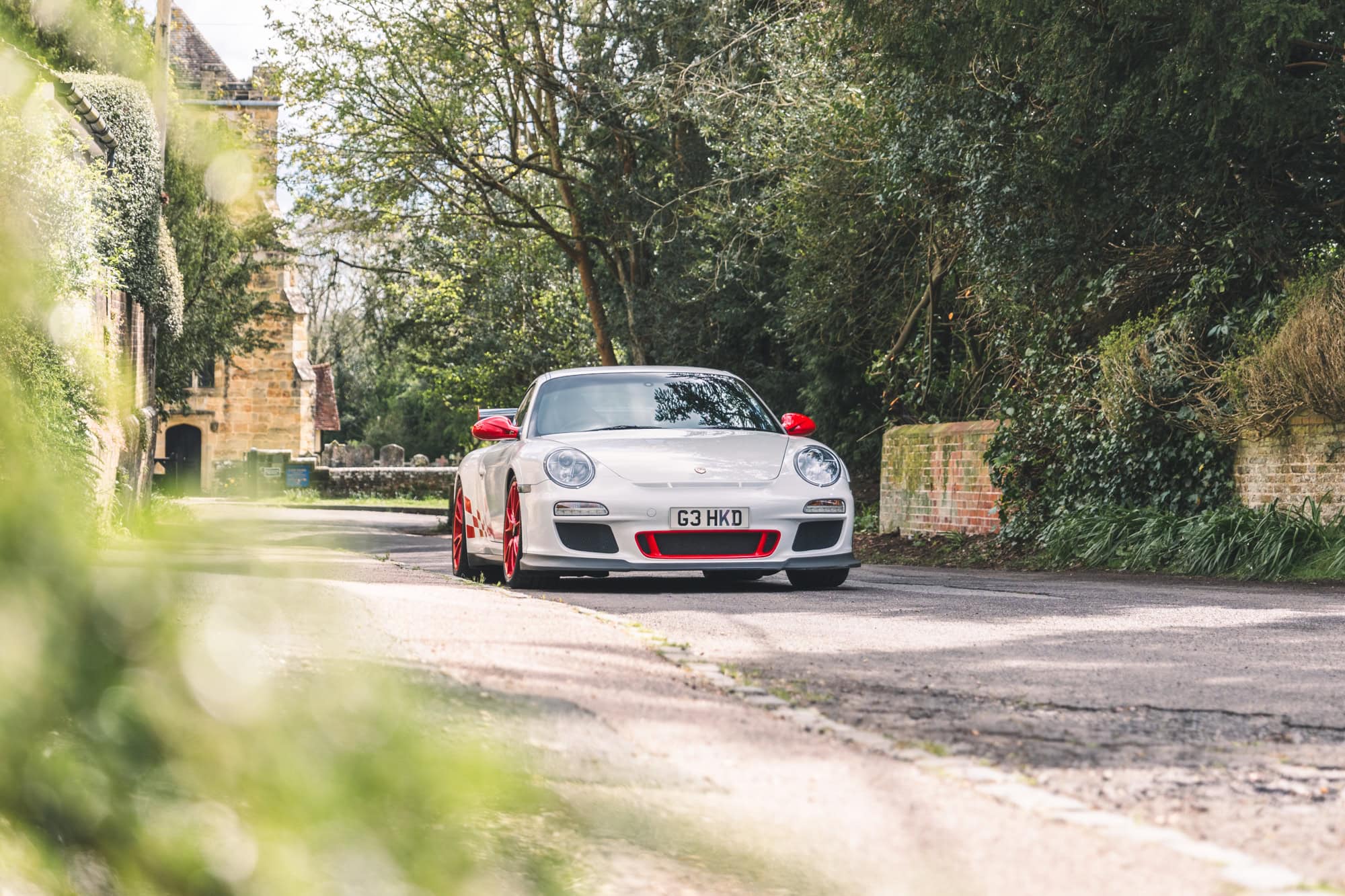 A performance classic Porsche 997 GT3 RS in white and red maintained and serviced by Hero Motor Company parked in a village in East Sussex.