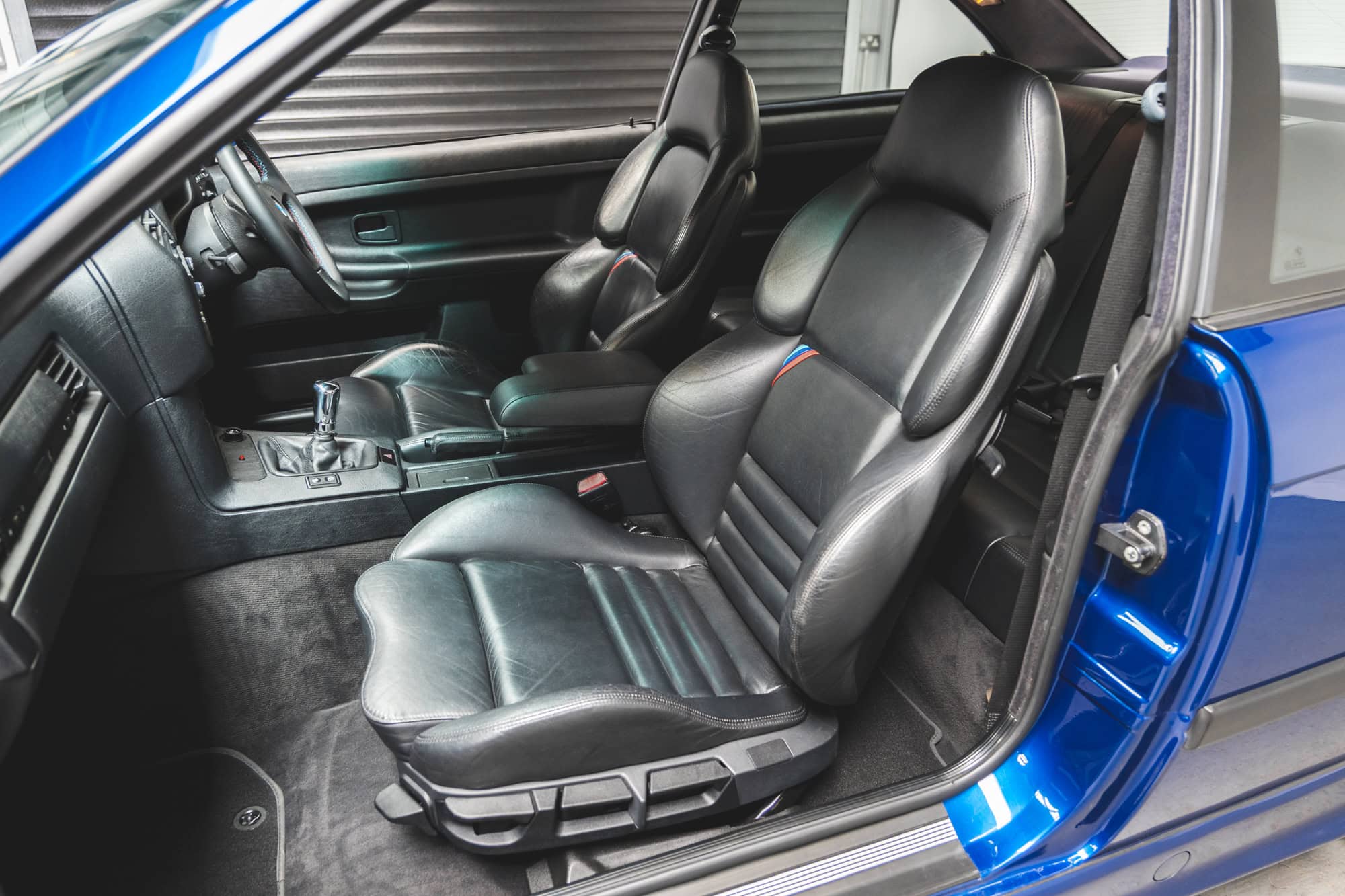 Nearside black leather interior showing centre console and BMW M stripes on BMW E36 M3 Avus Blue Metallic.