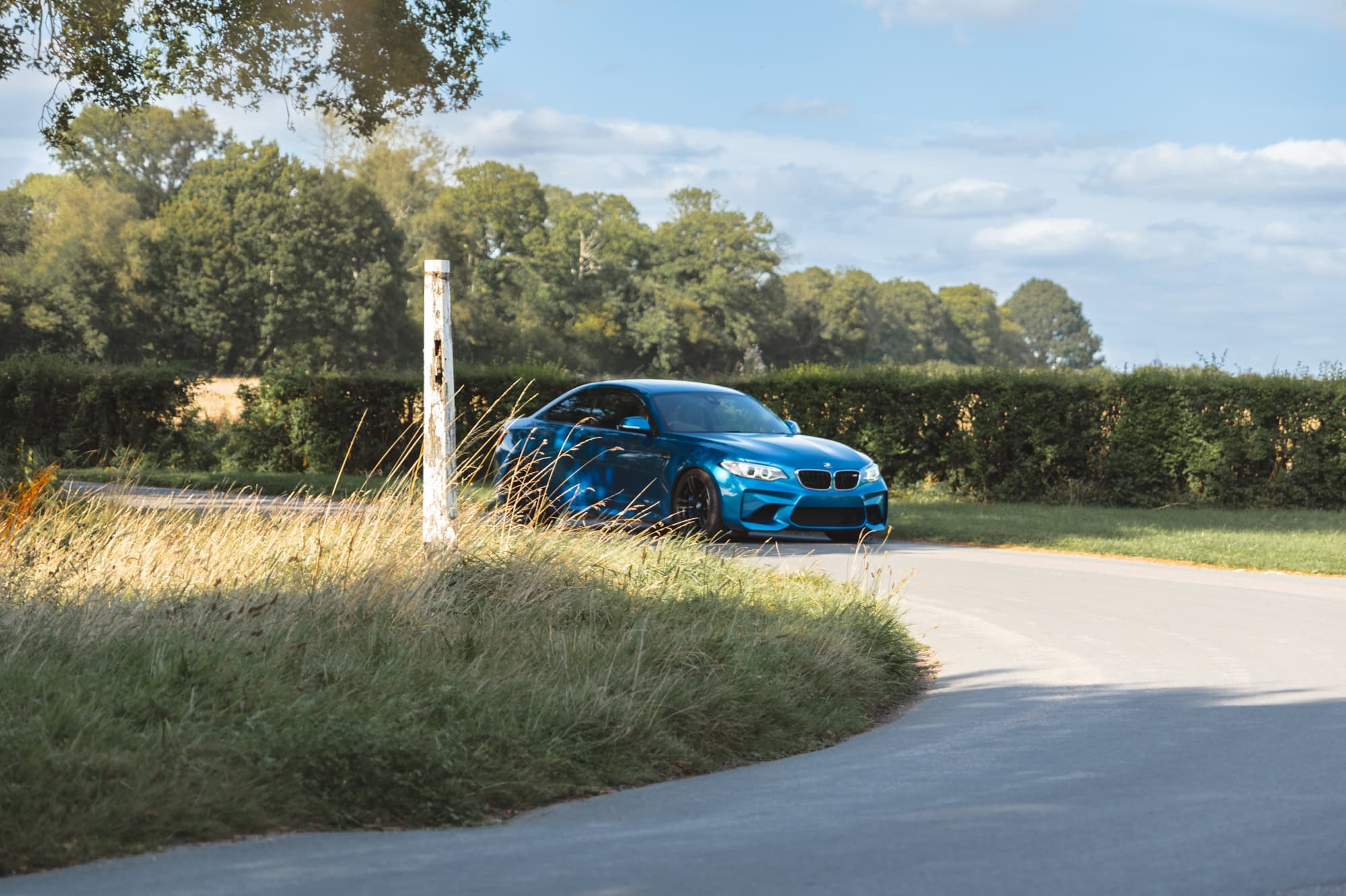 A BMW M2 taking a fast corner on a country road.