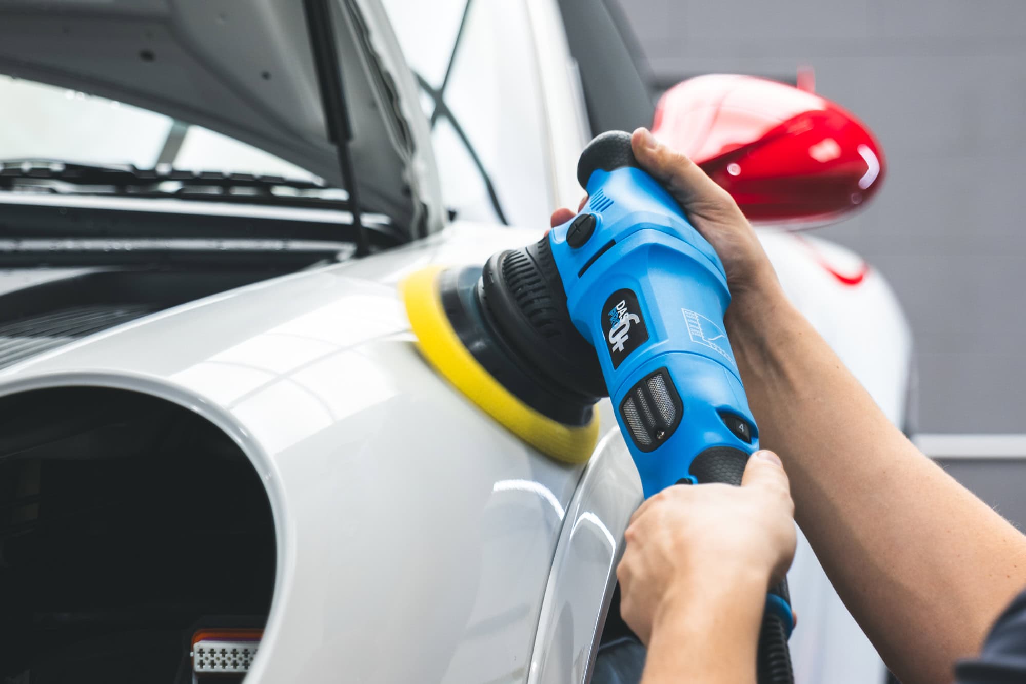 A car detailer machine polishes the front wing of a white Porsche 997 GT3 RS.