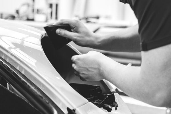 A car detailer wraps a Porsche 997 front wing in protective paint film.