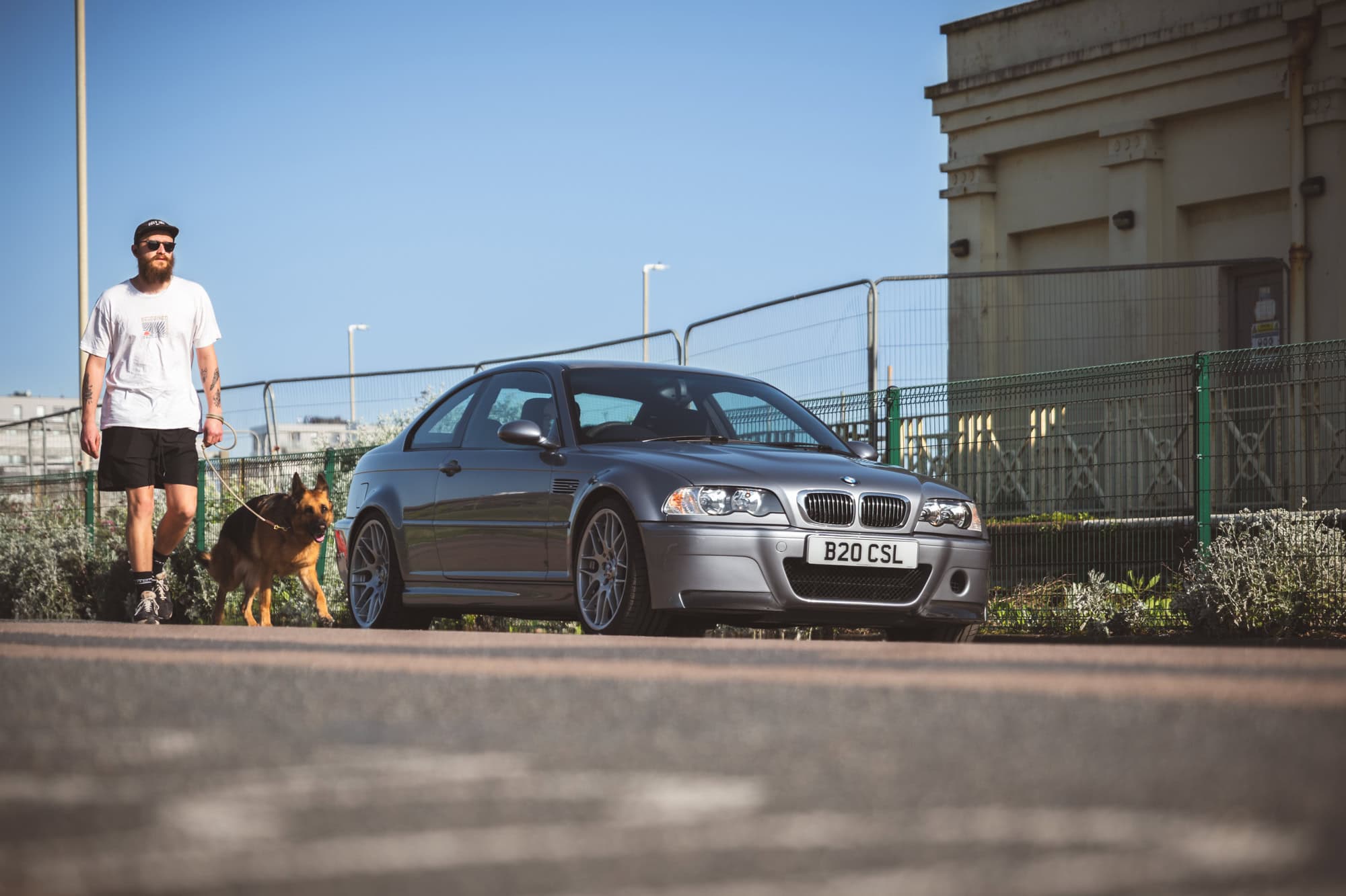 A trendy man walks his dog along side a grey BMW E46 M3 CSL on Brighton seafront.