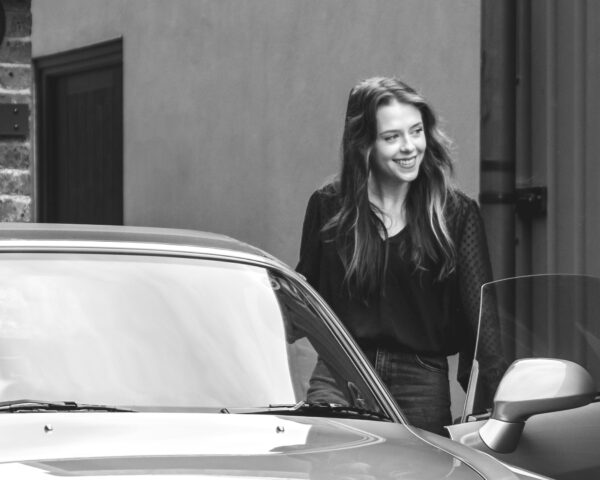 A black and white close up of a young professional woman steps into a blue Honda S2000.