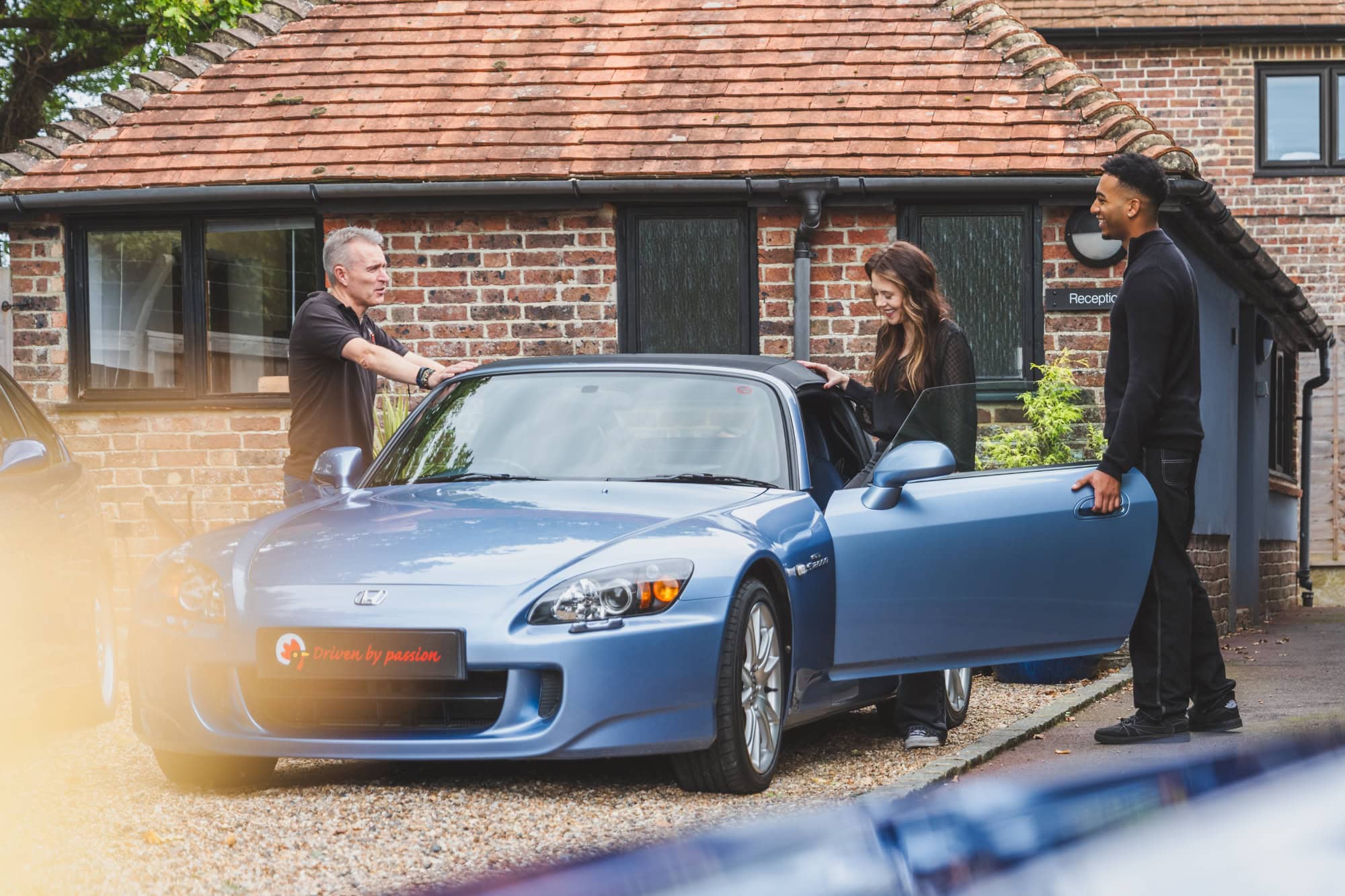 Jack shows a blue Honda S2000 convertible sports car to a young couple.