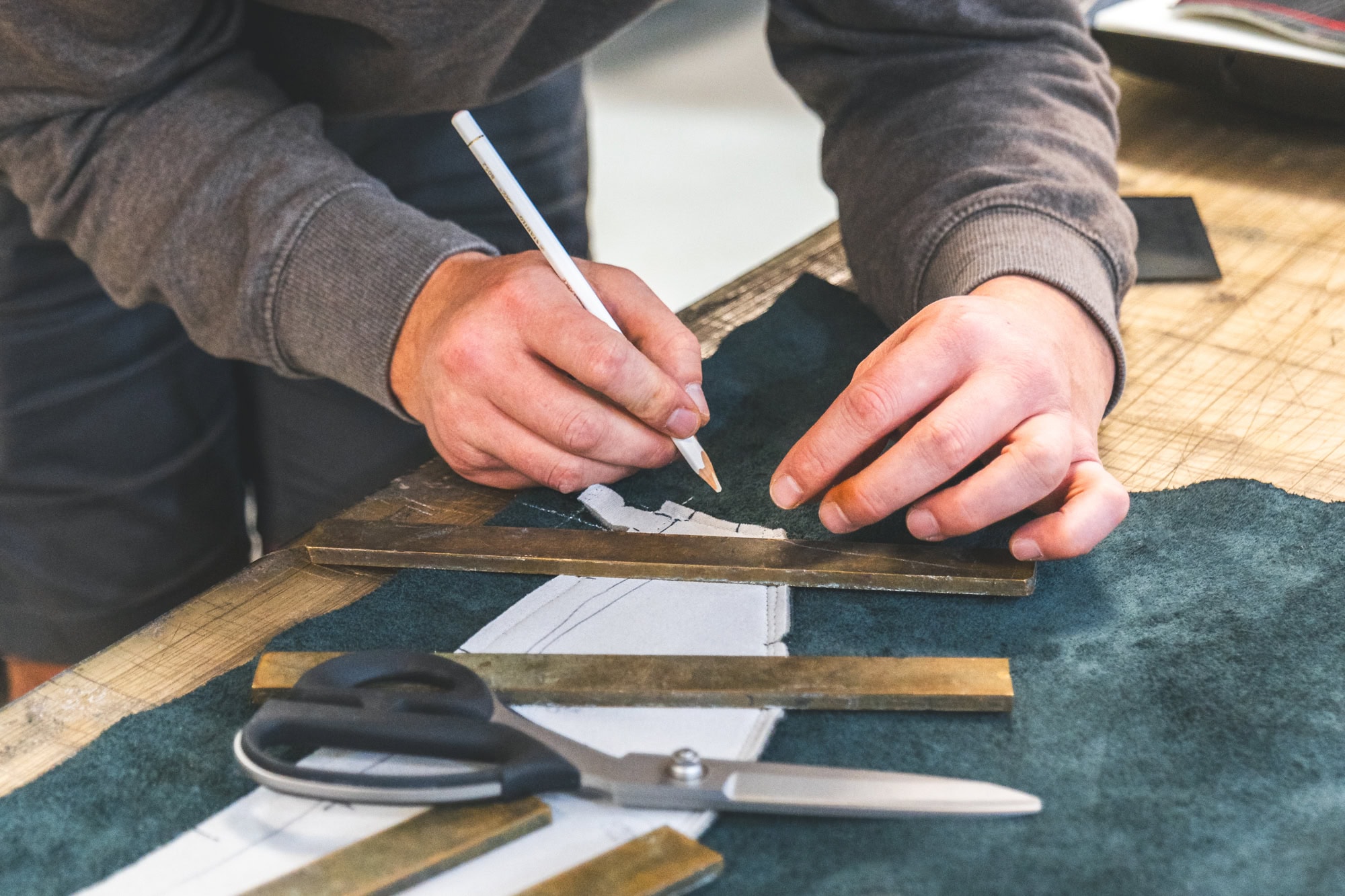 An automotive upholsterers hands holding a chalk pencil and tools on a workbench.