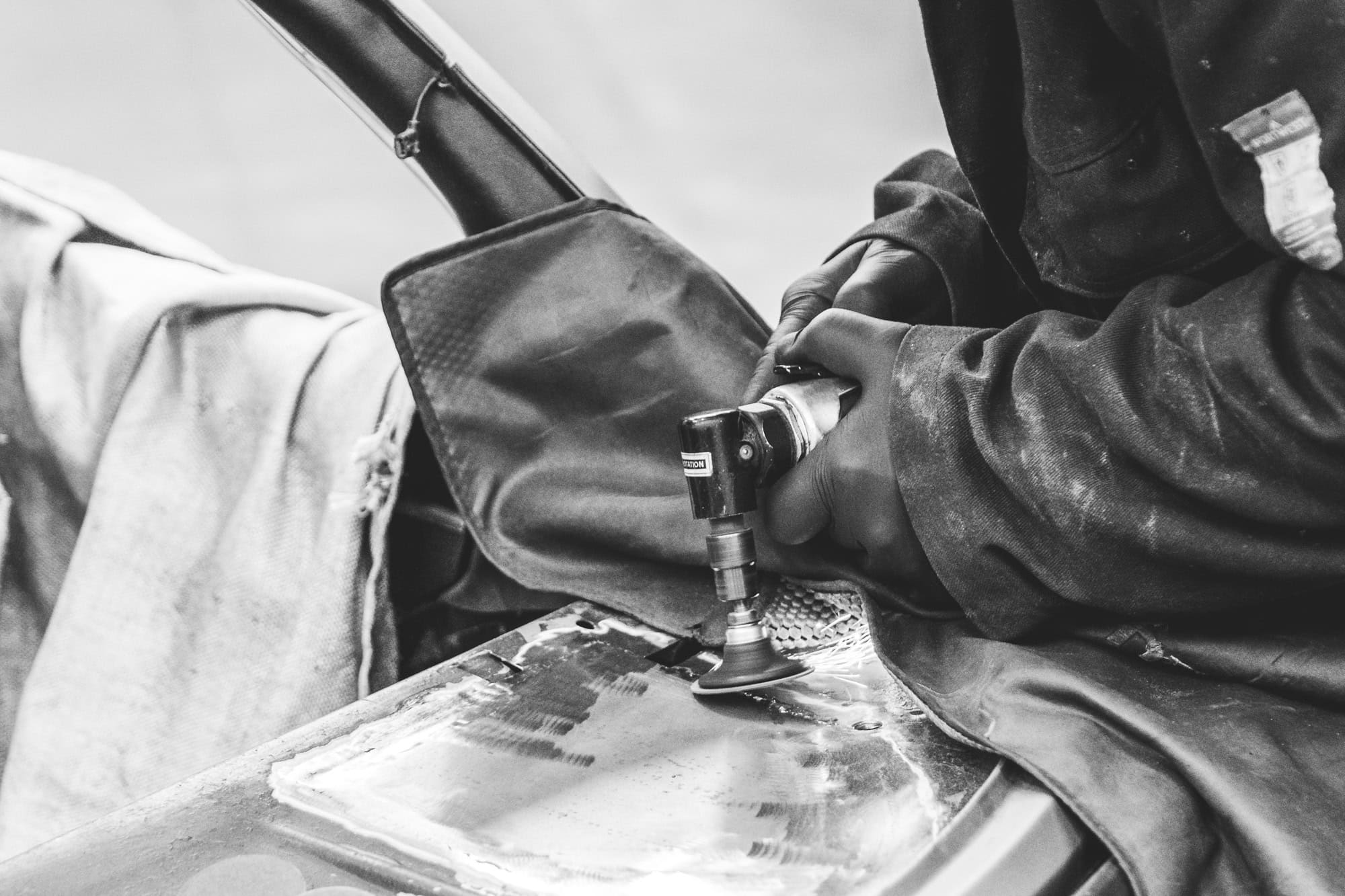 A mechanic uses air tools to grind back a weld on car bodywork.