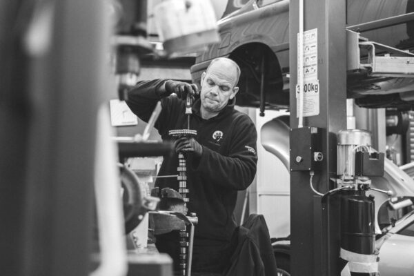 A mechanic works on the camshaft of a BMW in a busy workshop.