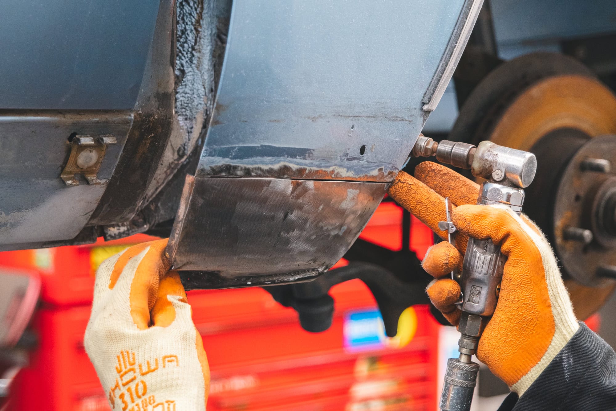 A mechanic holds up a body repair metal plate to a car to check fitment.