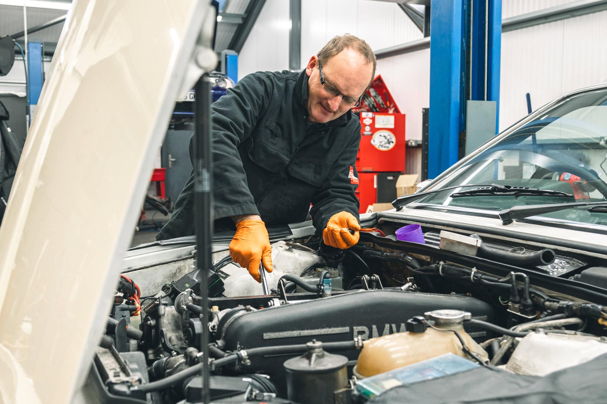 An experienced mechanic services the engine of a BMW M635 in a workshop.