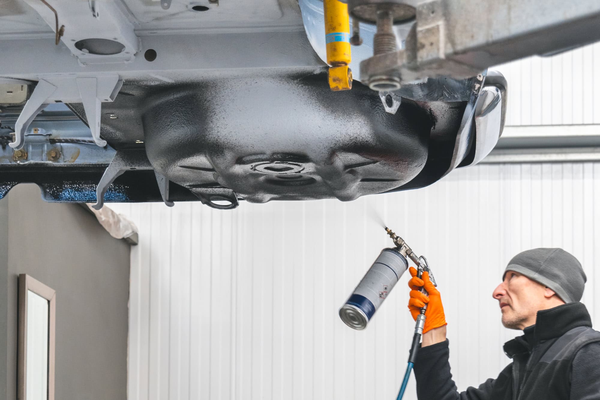 A specialist mechanic sprays dinitrol cavity protection wax on the underside of a BMW.