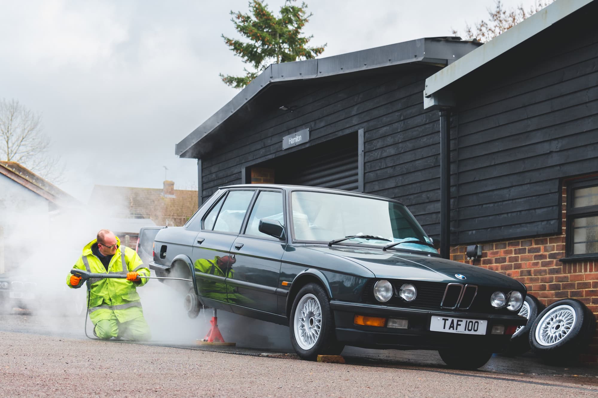 A mechanic steam cleans the underside of a BMW E28 M5 saloon.