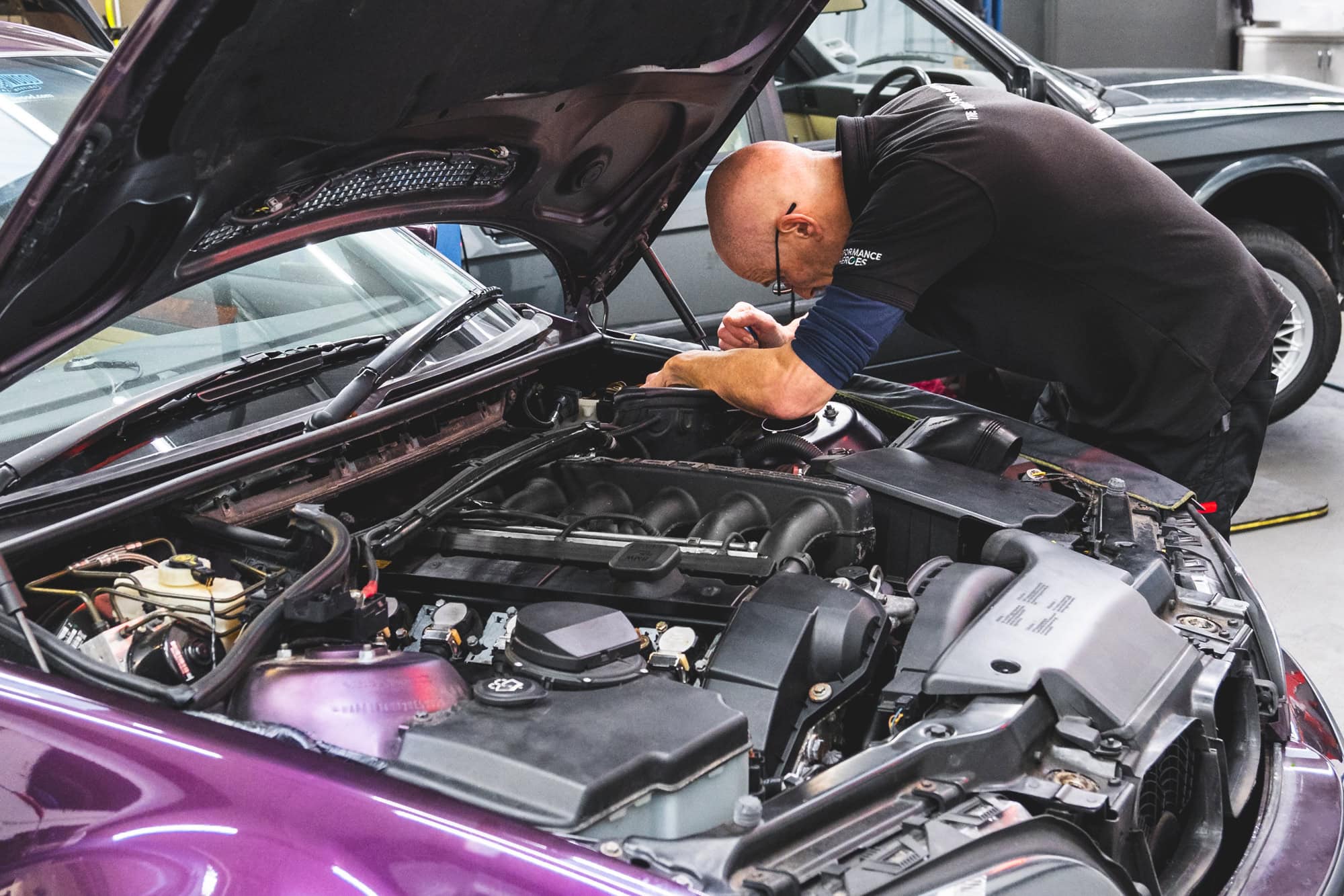 A skilled and experienced mechanic diagnoses an electrical issue on a purple BMW E46 Alpina B3.