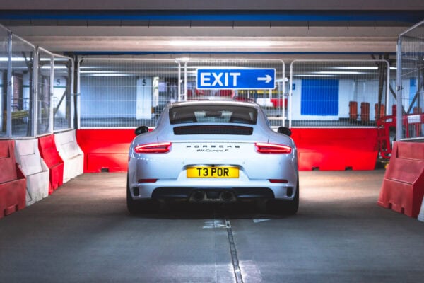 Rear view of a white Porsche 991 Carrera T in an underground car park with exit signage and bollards.