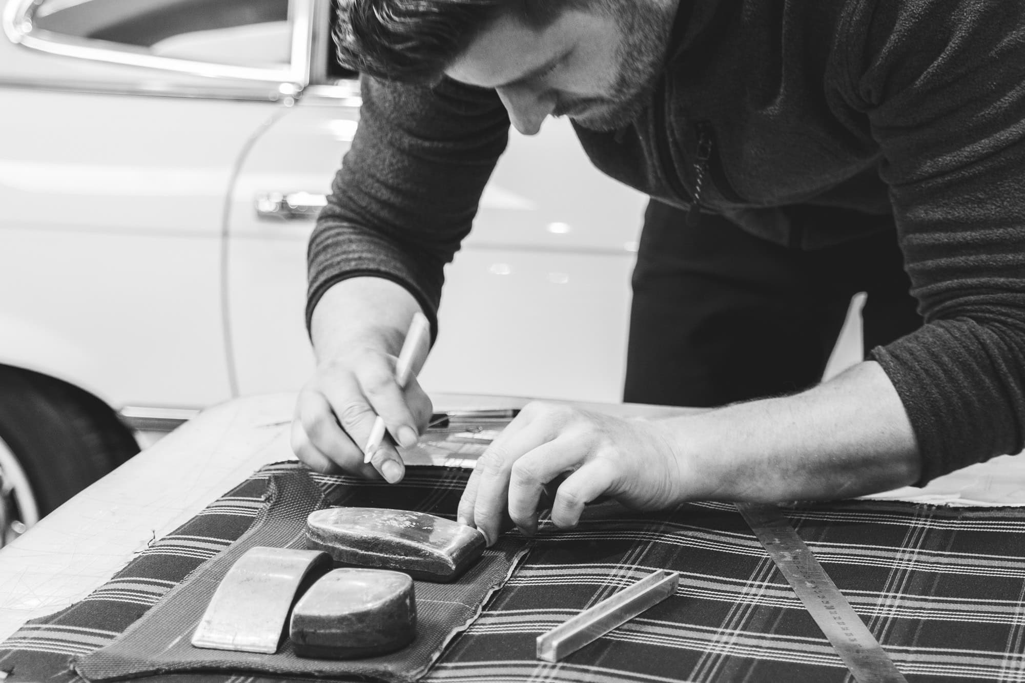 An automotive upholsterers hands holding a chalk pencil and tools on a workbench marking up fabric.