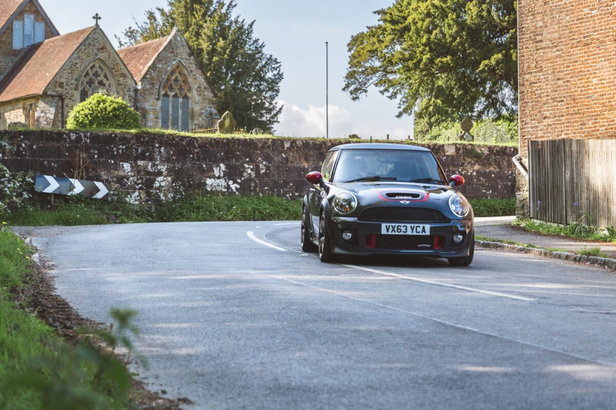 A grey Mini GP 2 Cooper S driving around a corner with a church in the background.