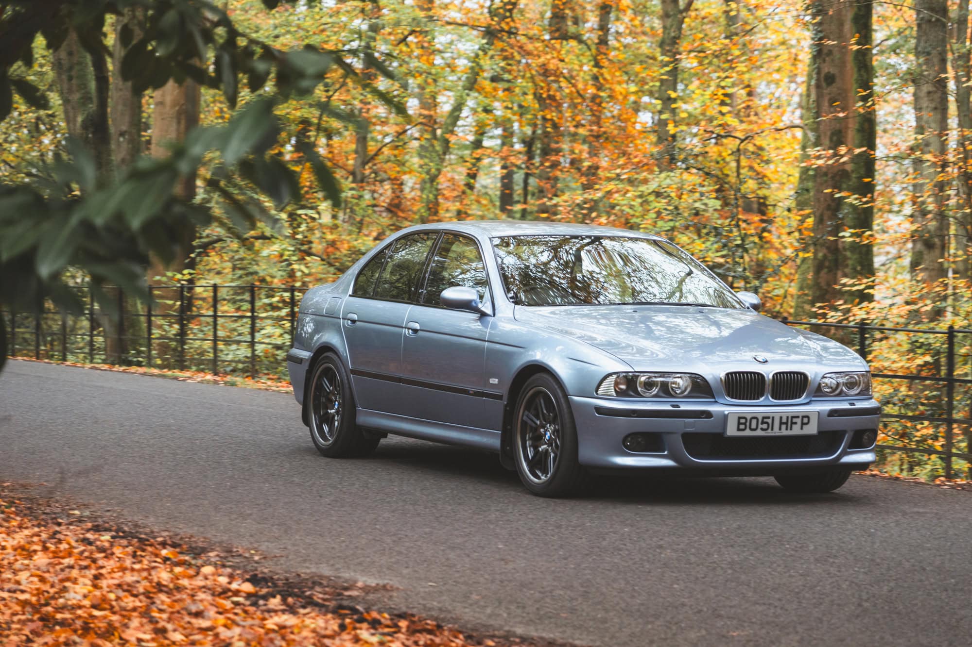 A BMW E39 M5 in Silverstone blue drives through autumn woodland.