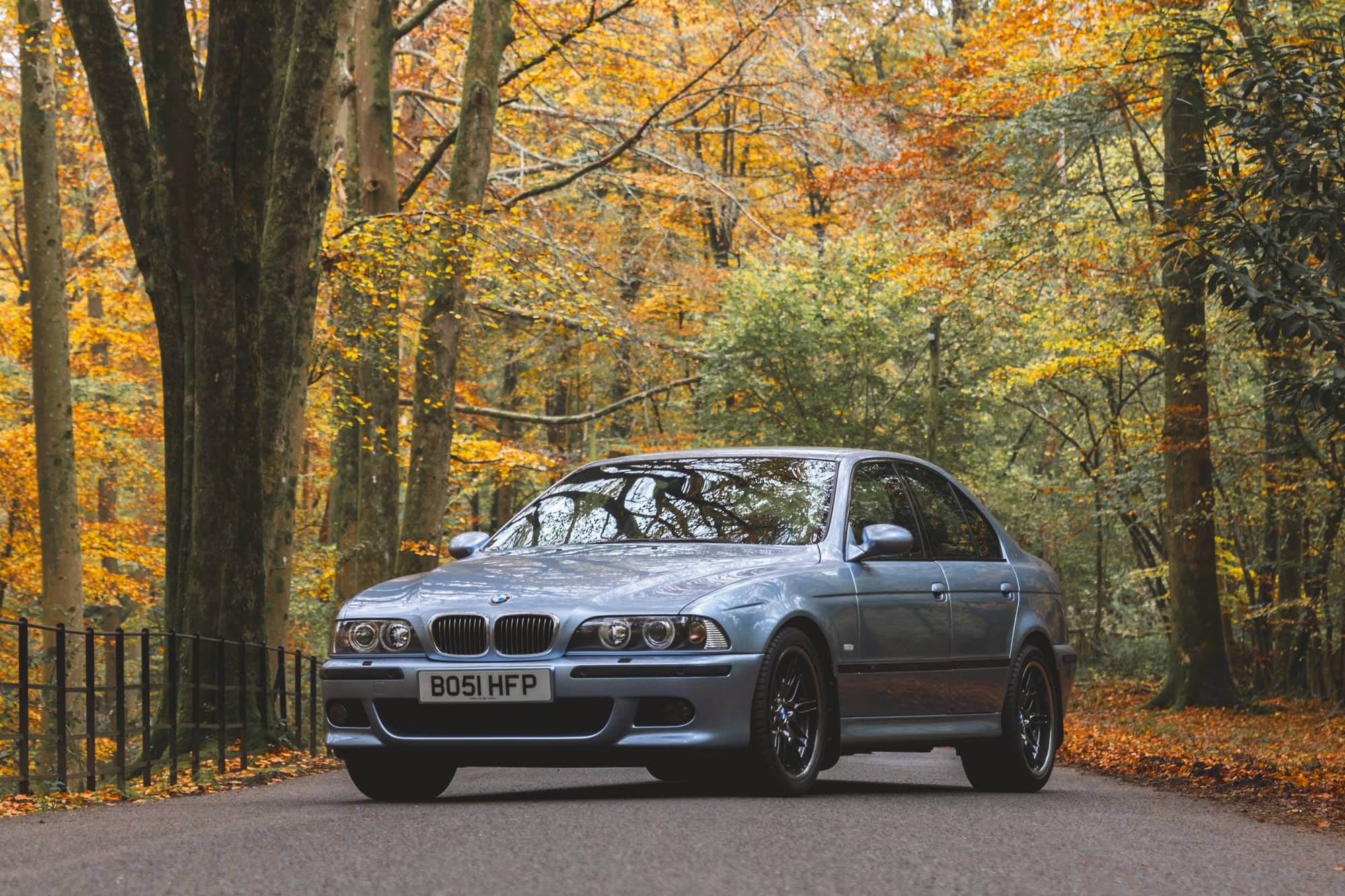 A Silverstone blue BMW E39 M5 parked on an autumn forest road.