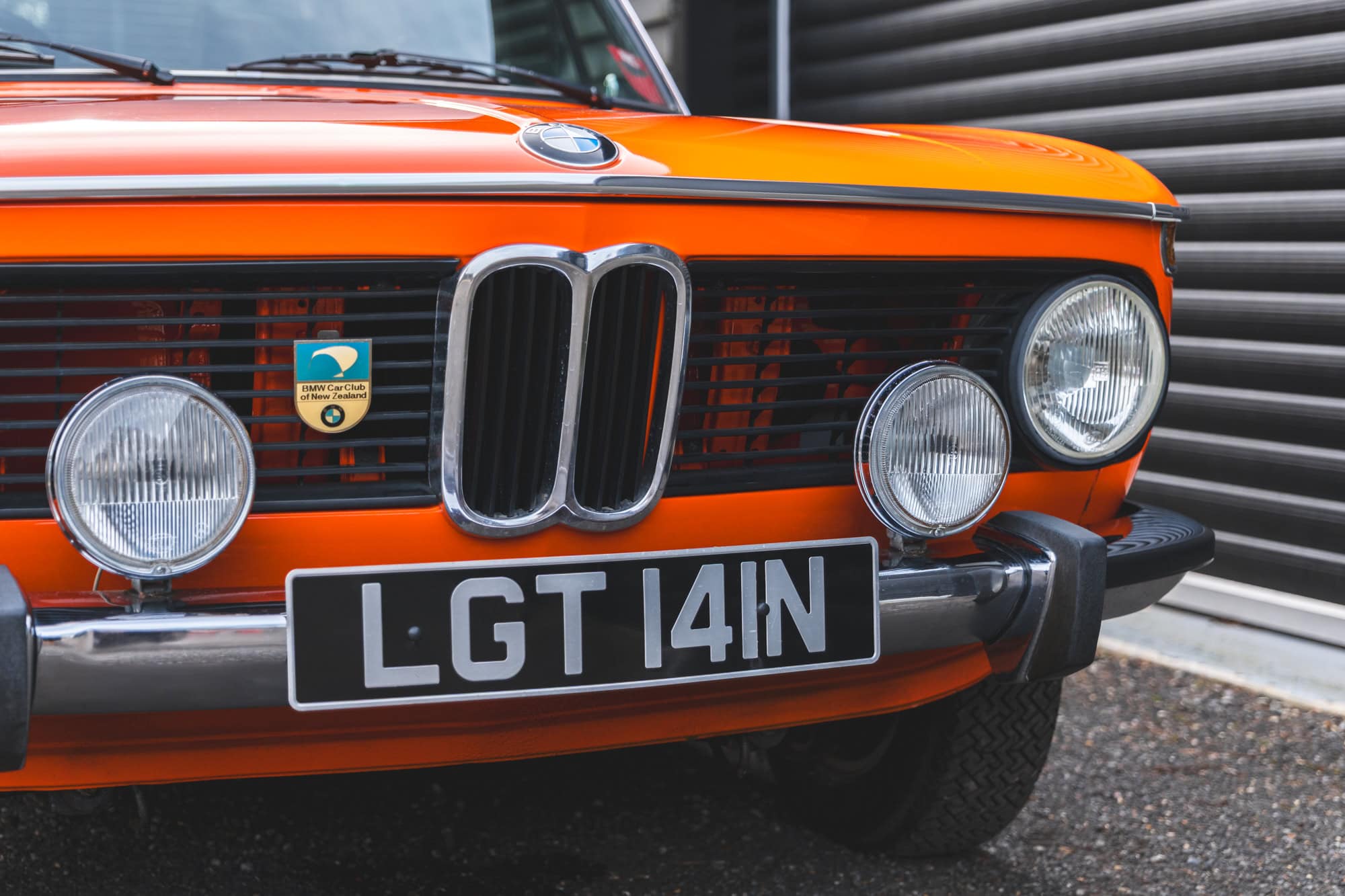 Front chrome bumper headlamps and BMW badge on BMW 2002 tii Inka Orange.