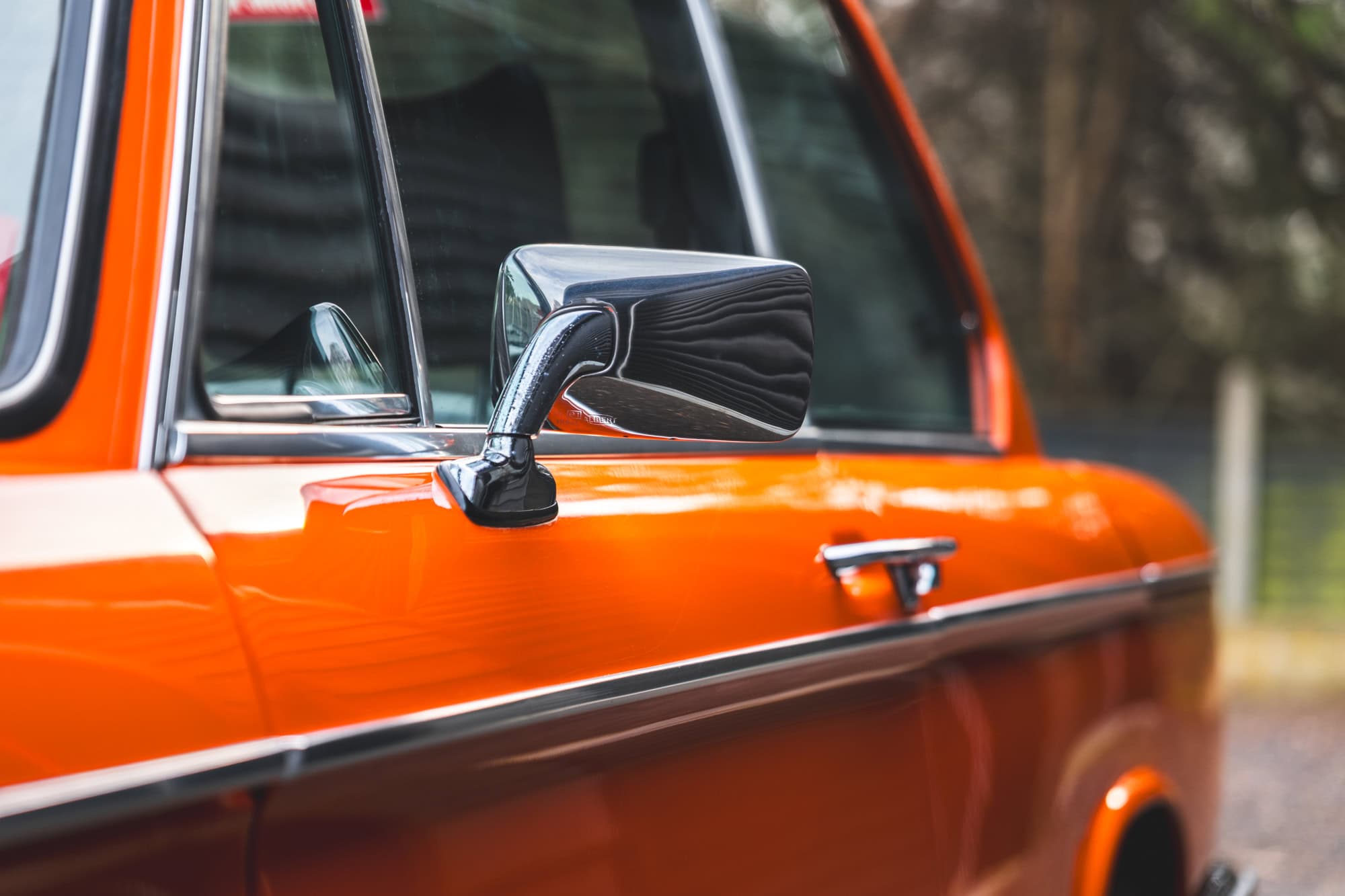 Nearside wing mirror showing chrome trim and matching door handle on BMW 2002 tii Inka Orange.