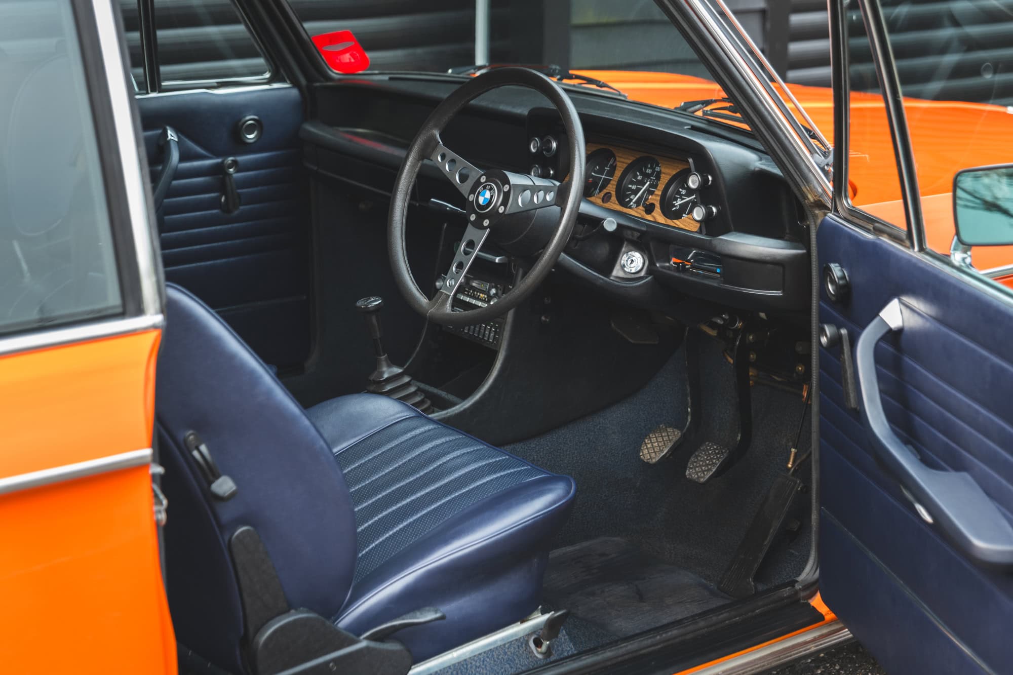 Offside view into leather interior showing centre console and steering wheel on a BMW 2002 tii Inka Orange.