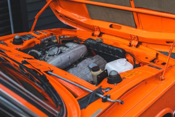 View of open bonnet and engine bay on BMW 2002 tii Inka Orange.