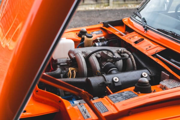 View of open bonnet and engine bay on BMW 2002 tii Inka Orange.