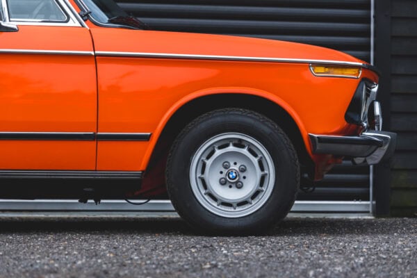 Close view of offside front wheel showing indicator and chrome bumper of BMW 2002 tii Inka Orange.