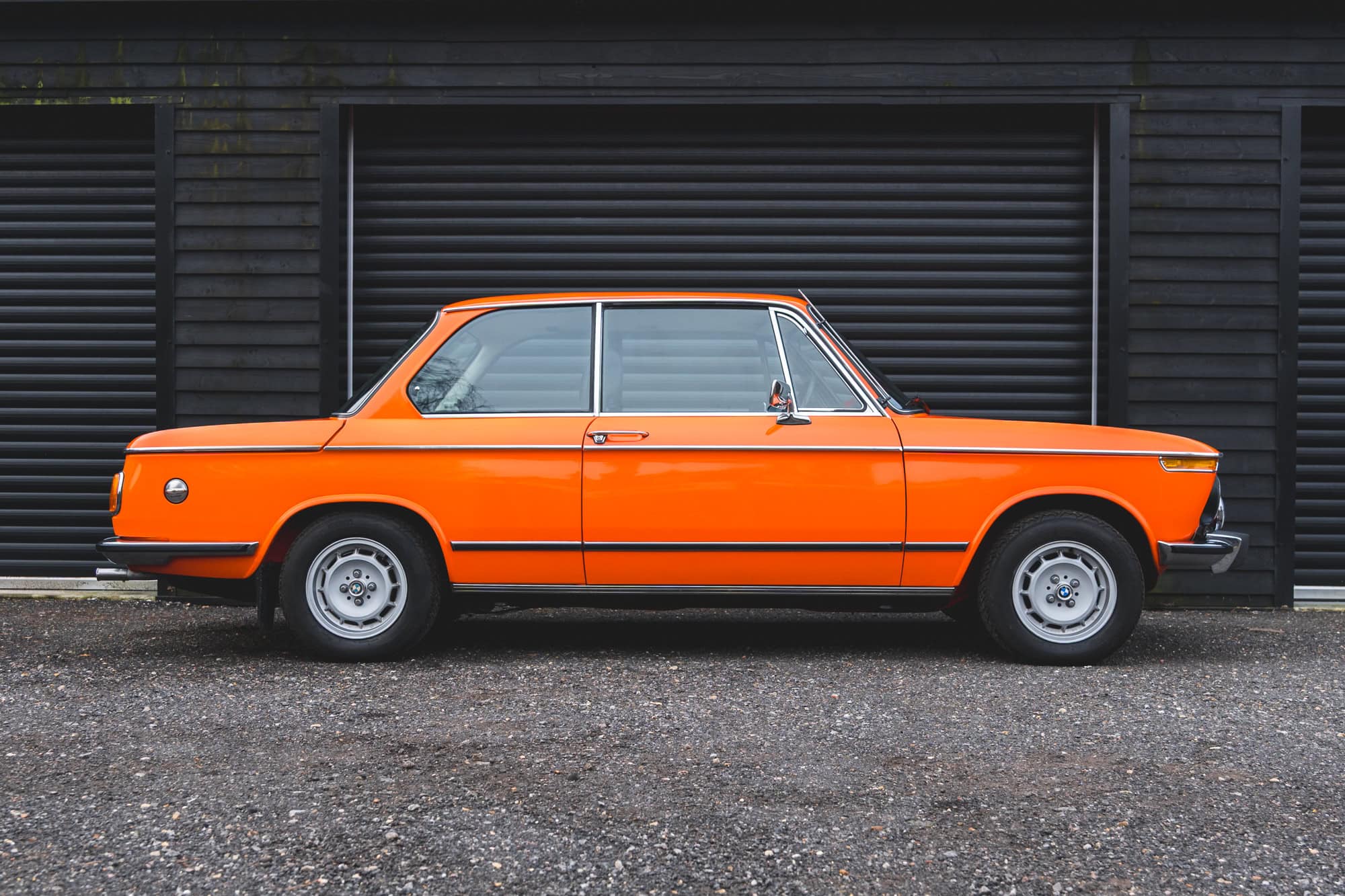 Offside exterior side view of BMW 2002 tii Inka Orange showing chrome and wheels.