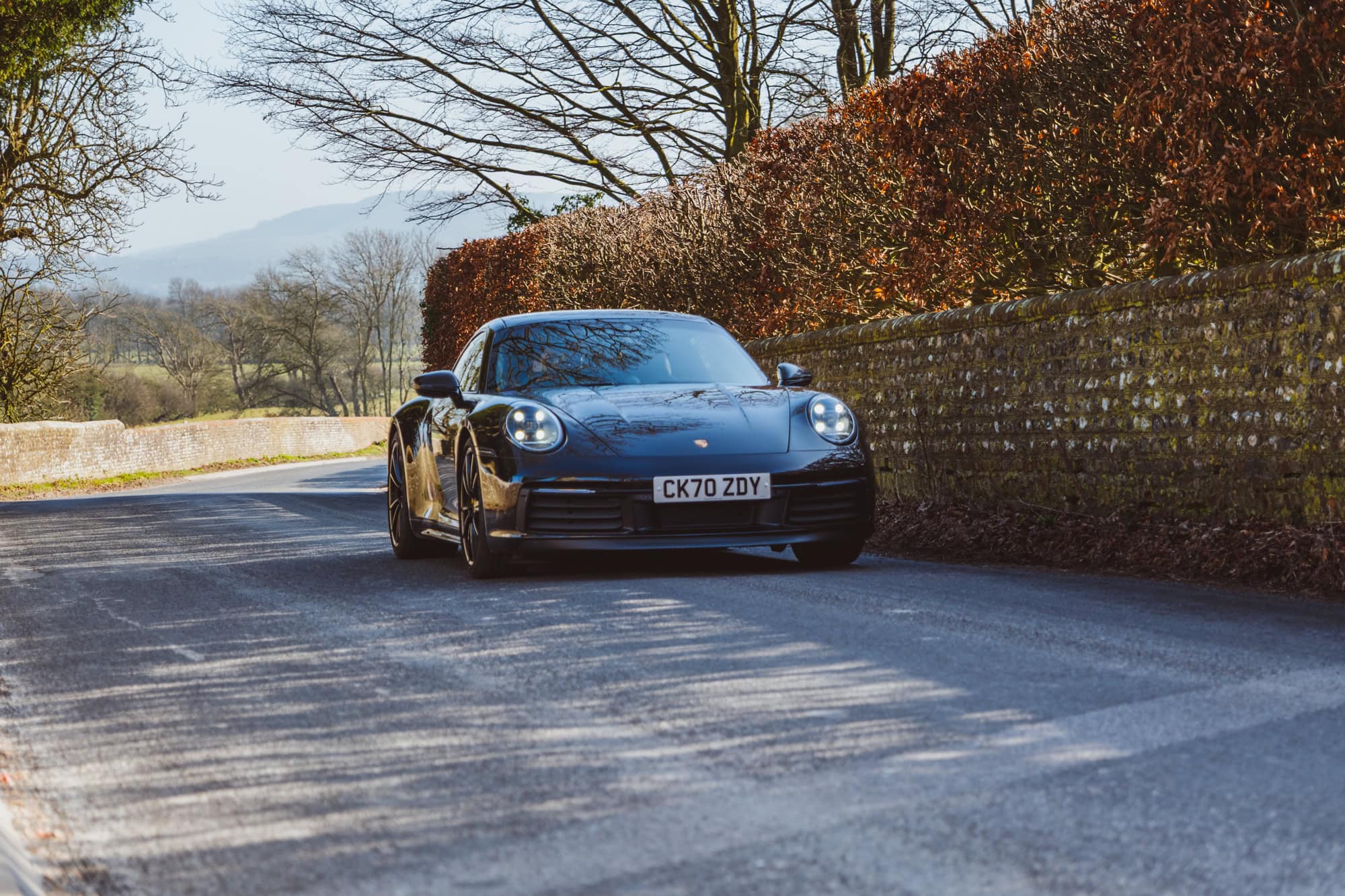 A black Porsche 992 driving fast on a country road.