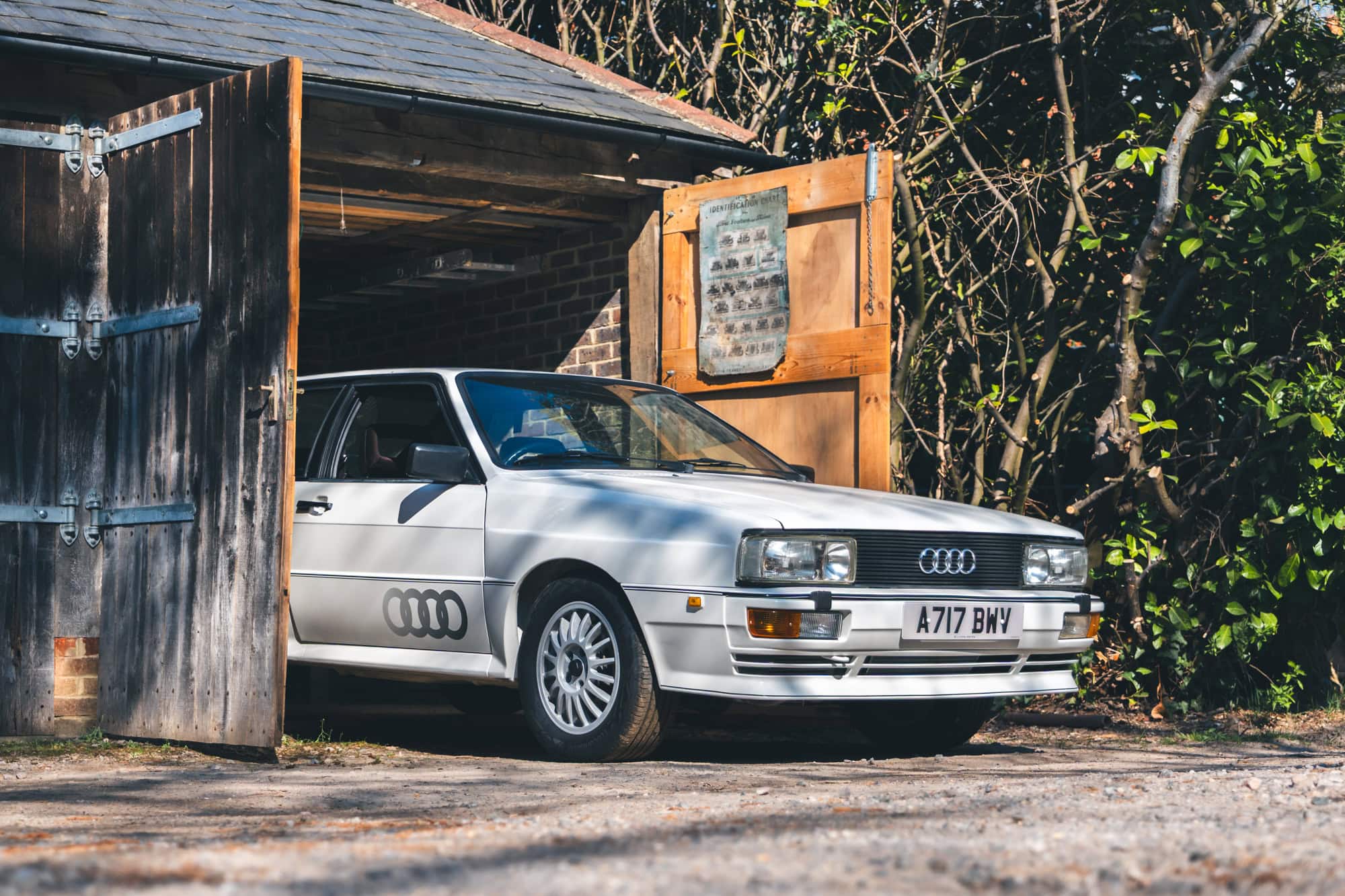 A white Audi Quattro emerging from a wooden barn.