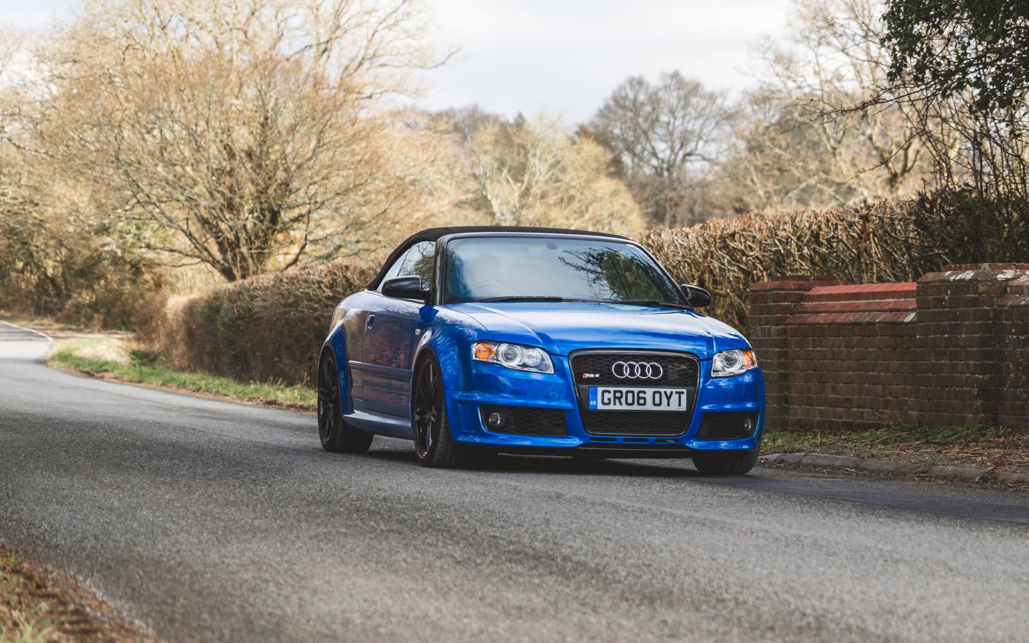 A Sprint Blue Audi RS4 cabriolet driving quickly over a rural bridge.