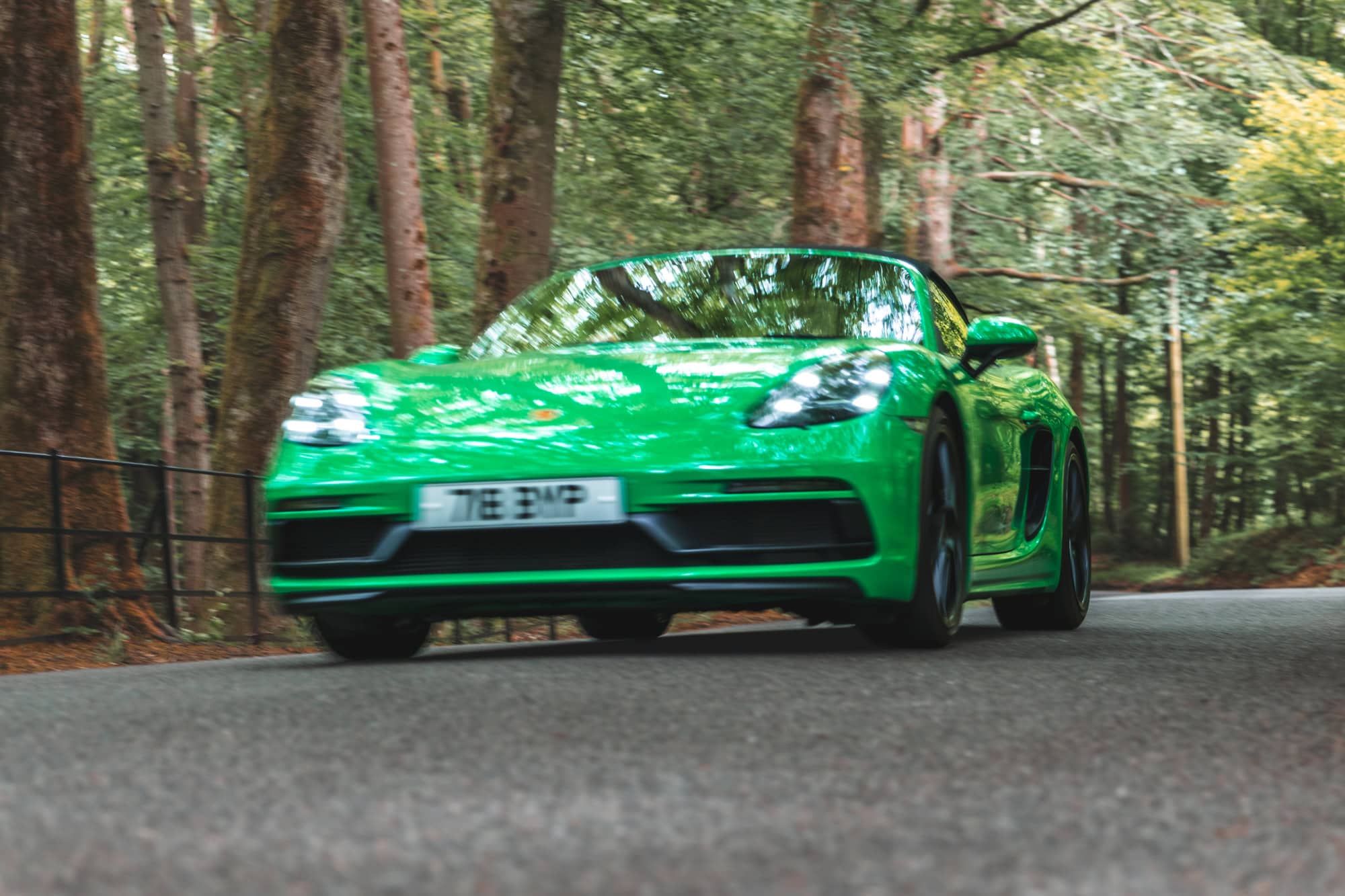 A Python Green Porsche Boxster 718 GTS in motion driving down a forest road.