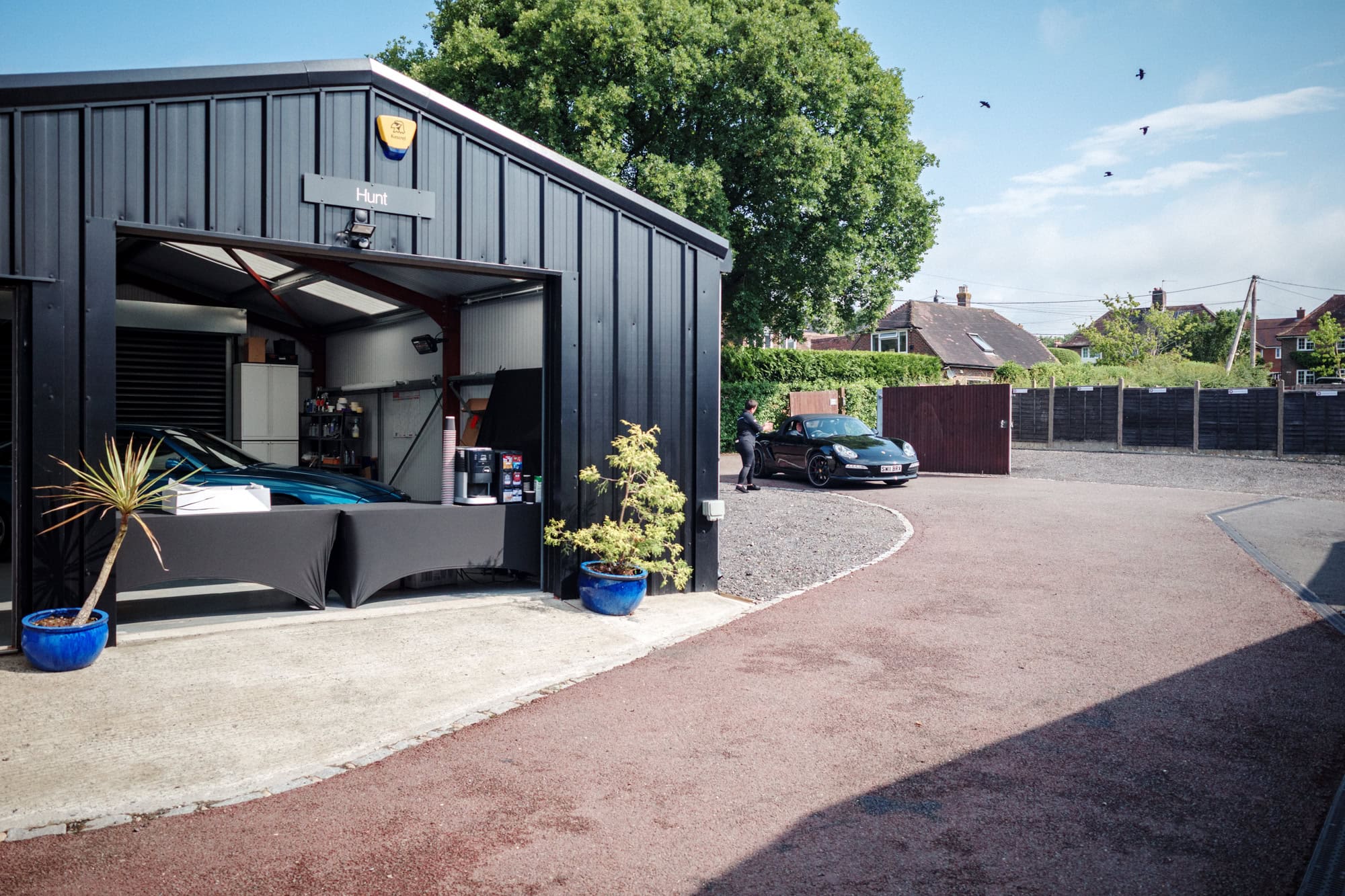 A wide view of the top yard at hero motor company as a black Porsche Boxster arrives.