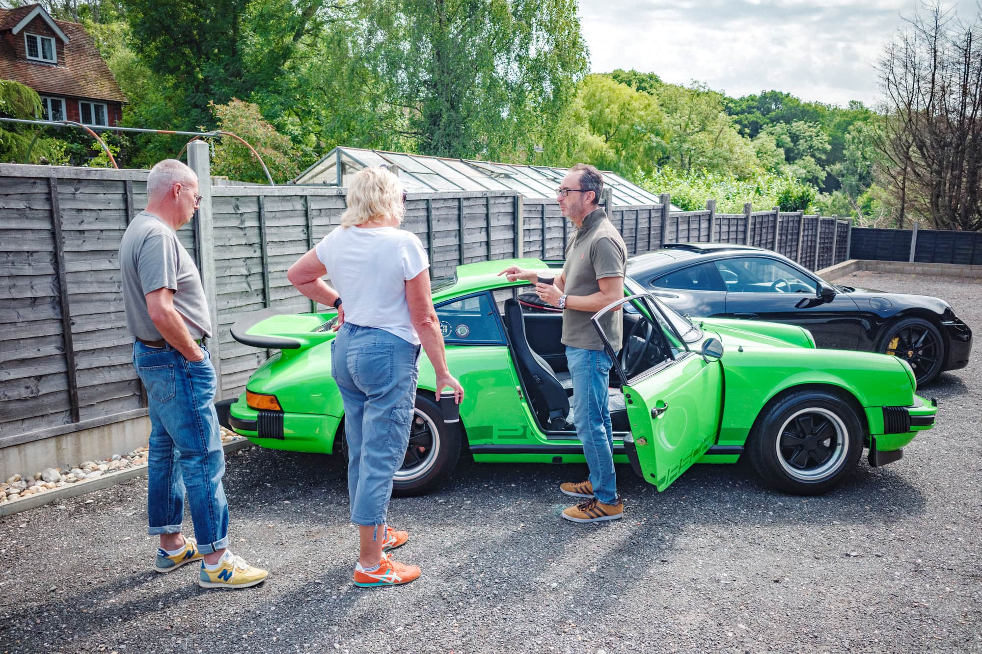 Three enthusiasts talk next to a well restored Porsche 930 in lime green.