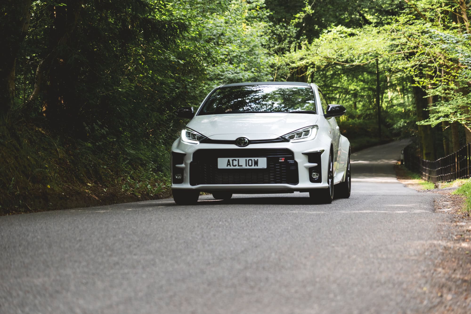 A white Toyota Yaris GR Four accelerating up a road in the countryside.