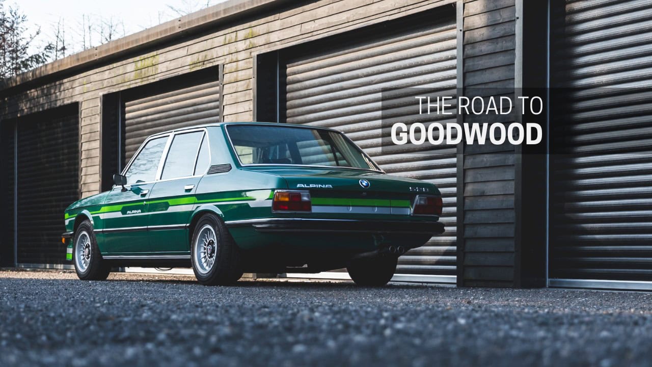 A jade green Alpina b6 528 saloon in front of black shutter doors.