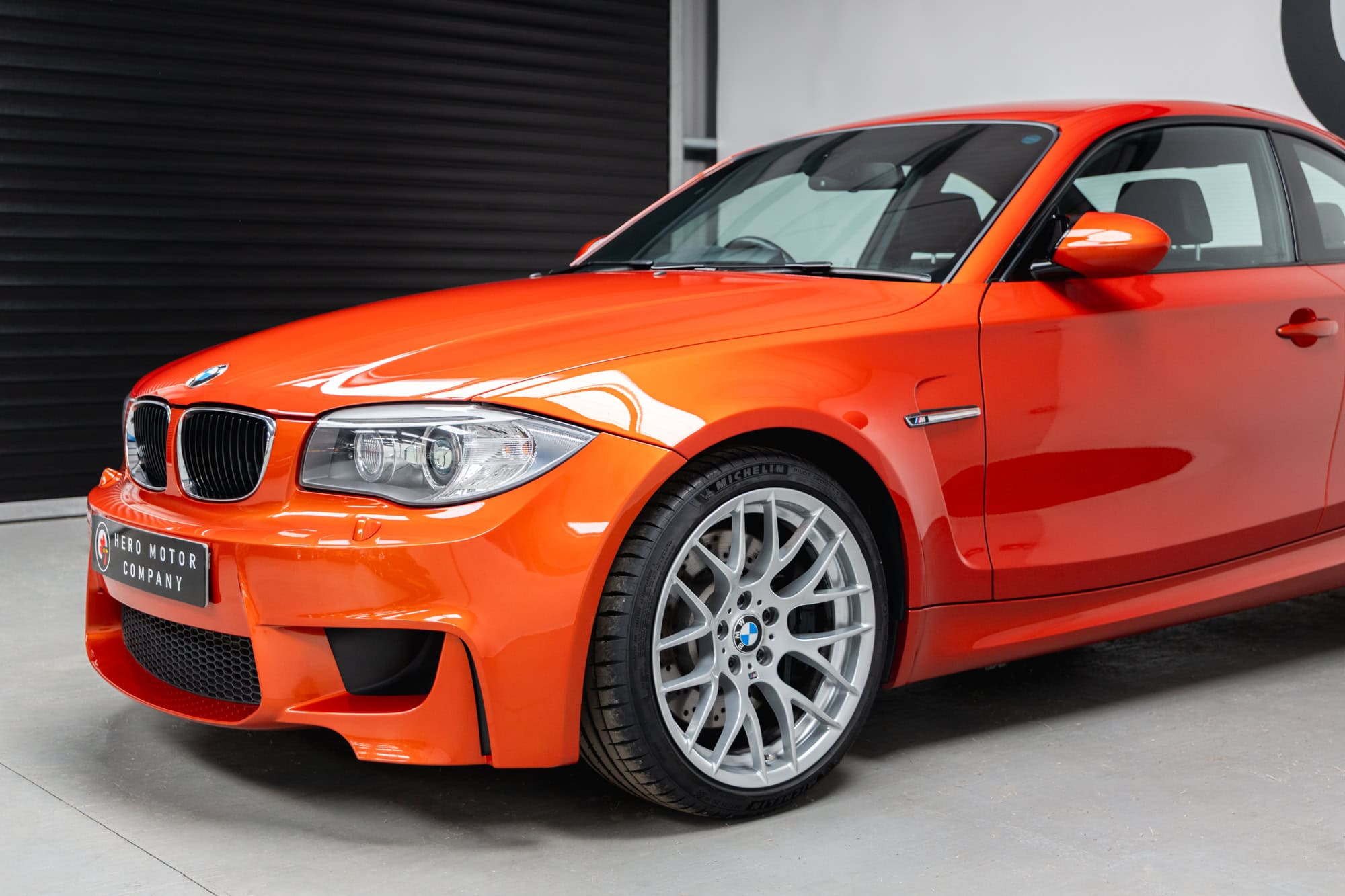 Nearside front exterior of BMW E82 1M Coupe Valencia Orange showing alloy wheels and chrome bumper