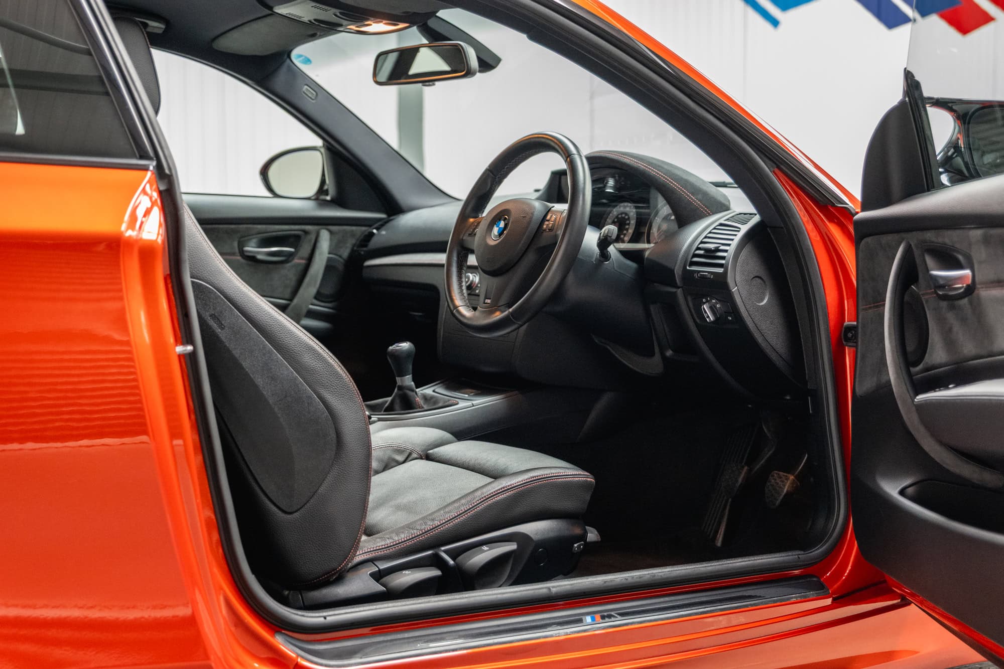 Offside interior view of black leather seat and steering wheel on BMW E82 1M Coupe Valencia Orange