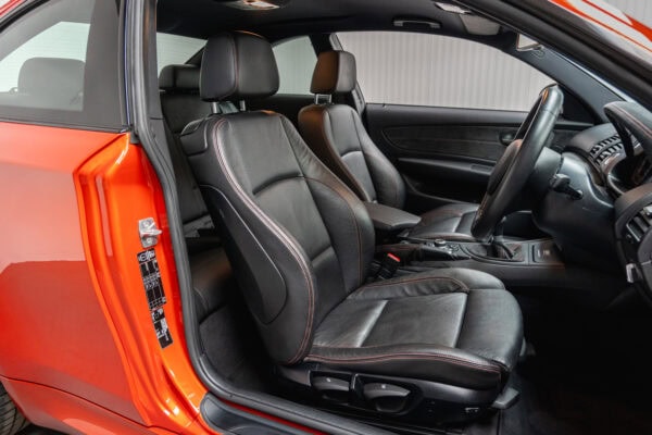Offside interior view of black leather interior showing steering wheel on BMW E82 1M Coupe Valencia Orange