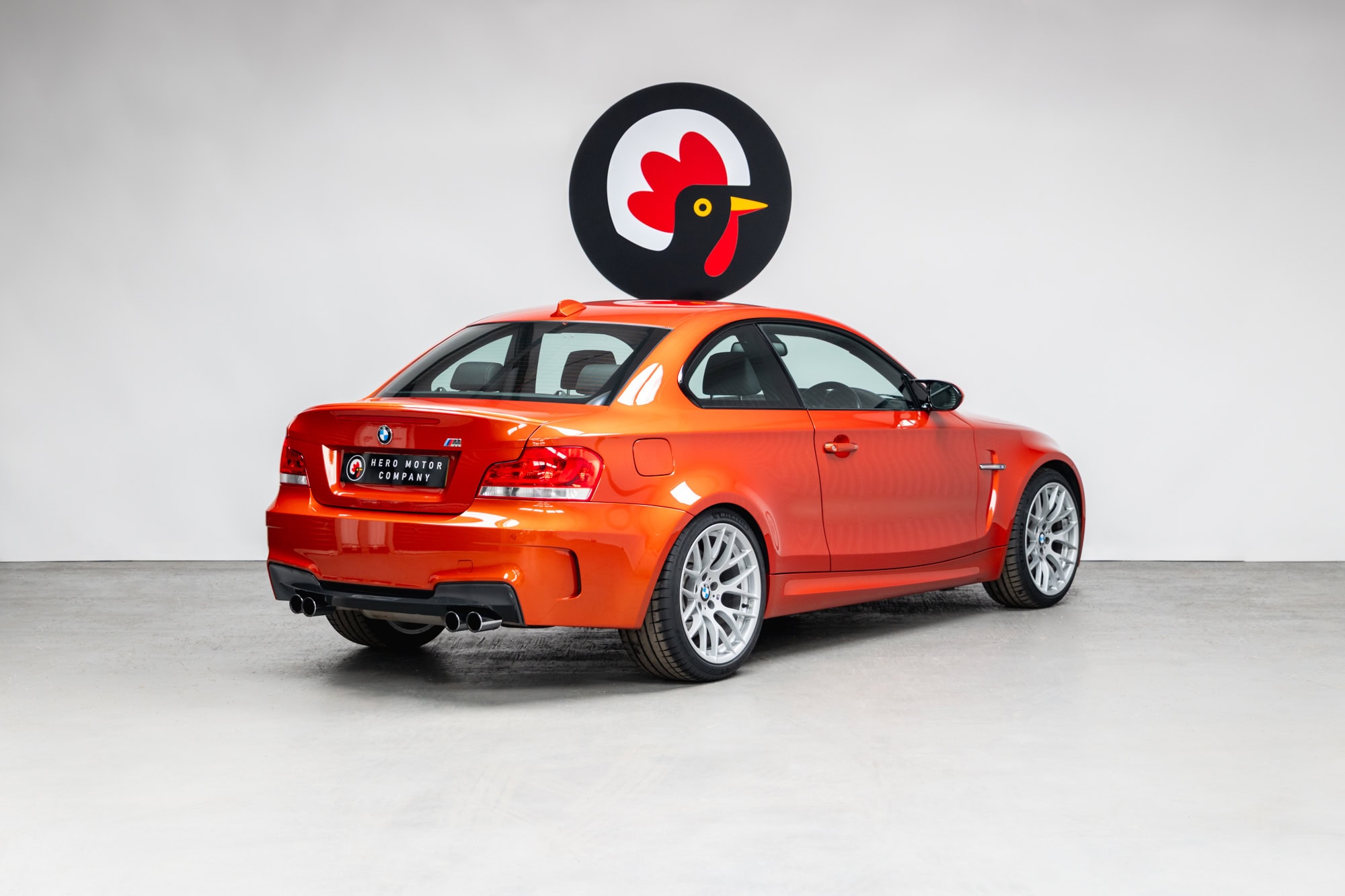 Rear offside exterior of BMW E82 1M Coupe Valencia Orange showing alloy wheels and rear exhaust tail pipes